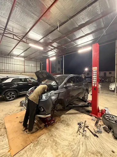 Mechanic working in the engine bay of a car on a two-post lift at night.